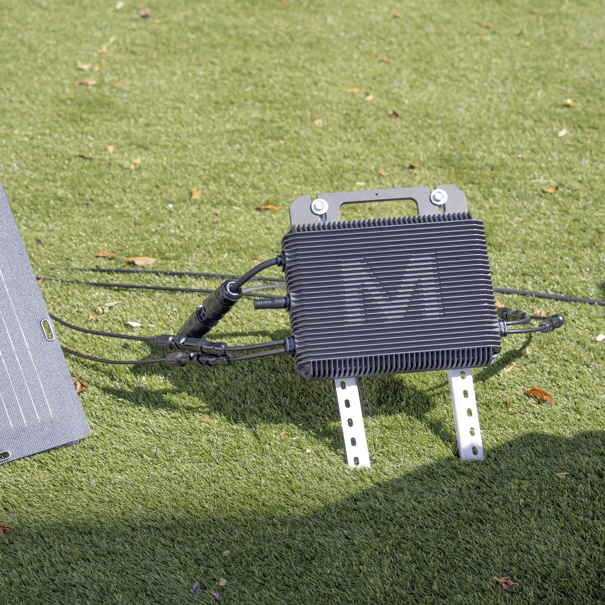 Mikrowechselrichter des Balkonkraftwerks an der Profilschiene montiert, daneben ein Solarmodul im Garten